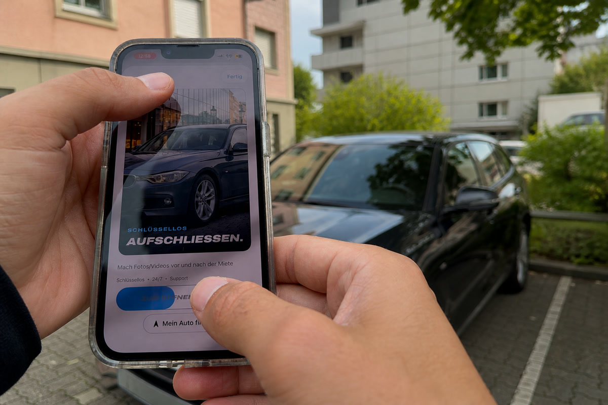 Zwei Hände halten ein Telefon mit der geöffneten DRAIV-App vor einem parkierten BMW